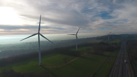 Wind-turbines-electric-power-generator-near-a-highway-misty-morning-aerial-drone
